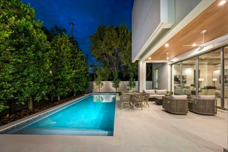 Lap pool beside a modern home with lounge patio at dusk