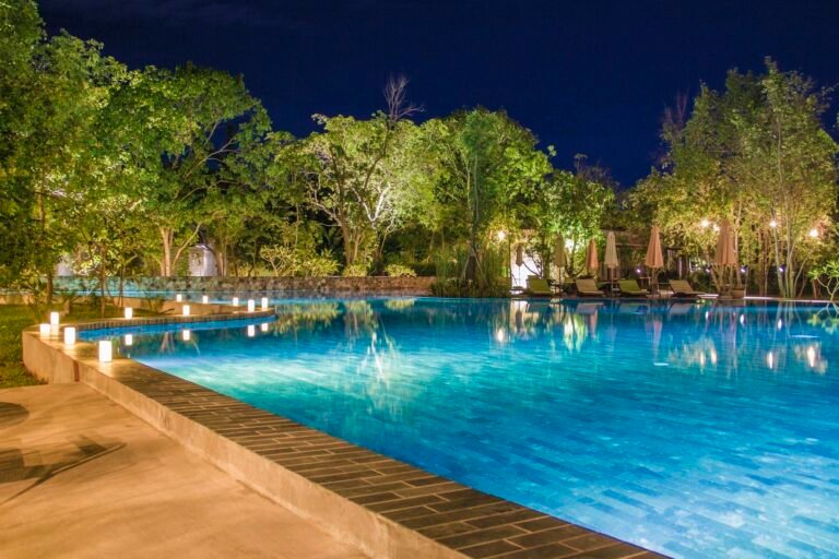 Lit infinity-edge pool at night surrounded by trees