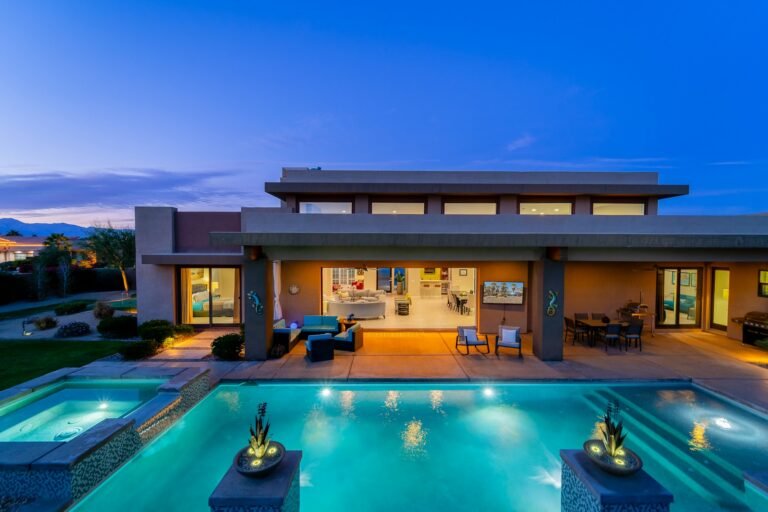 Modern desert home with lit pool, spa and fire bowls at dusk