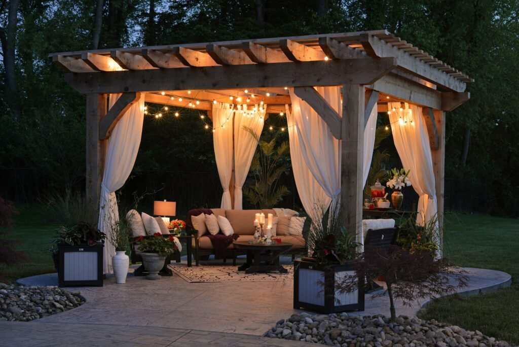 Lit wooden pergola with curtains and lounge seating at night
