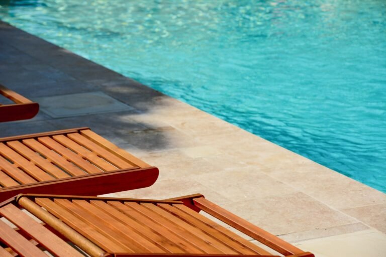 Stone pool deck with wooden lounge chairs beside pool