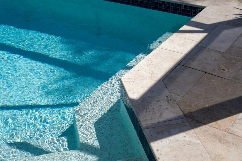 Travertine pool coping and steps beside clear blue water