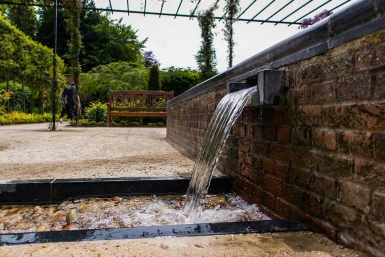 Water scupper spilling from brick wall into a pool